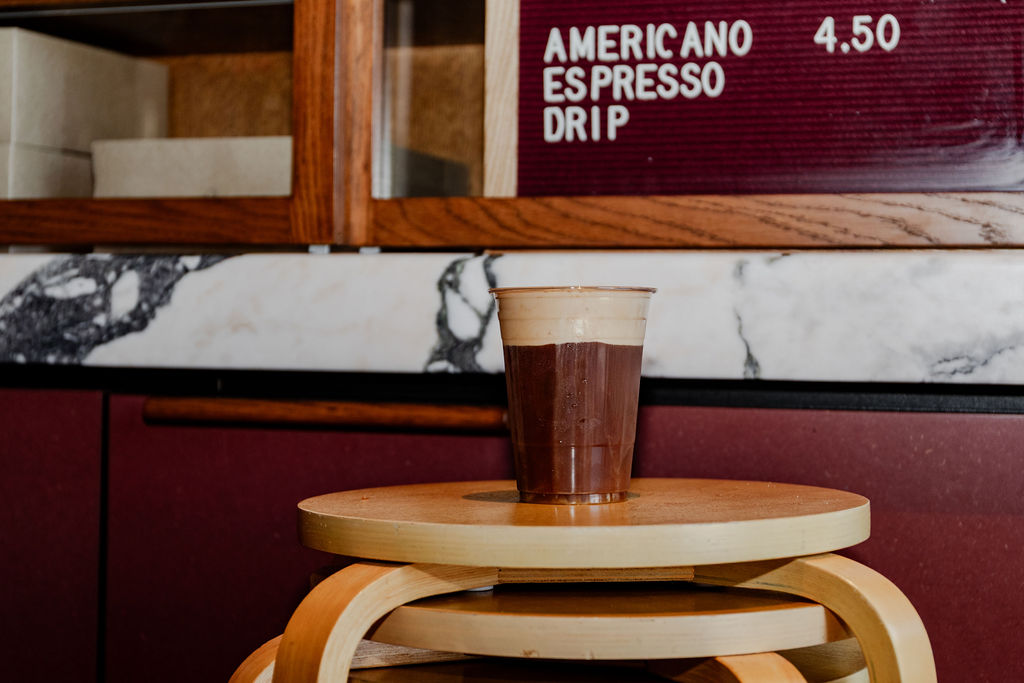 Cold brew on a stool below the menu board